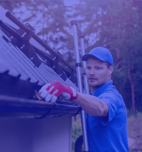 Man in blue uniform cleaning roof gutters with a tool.