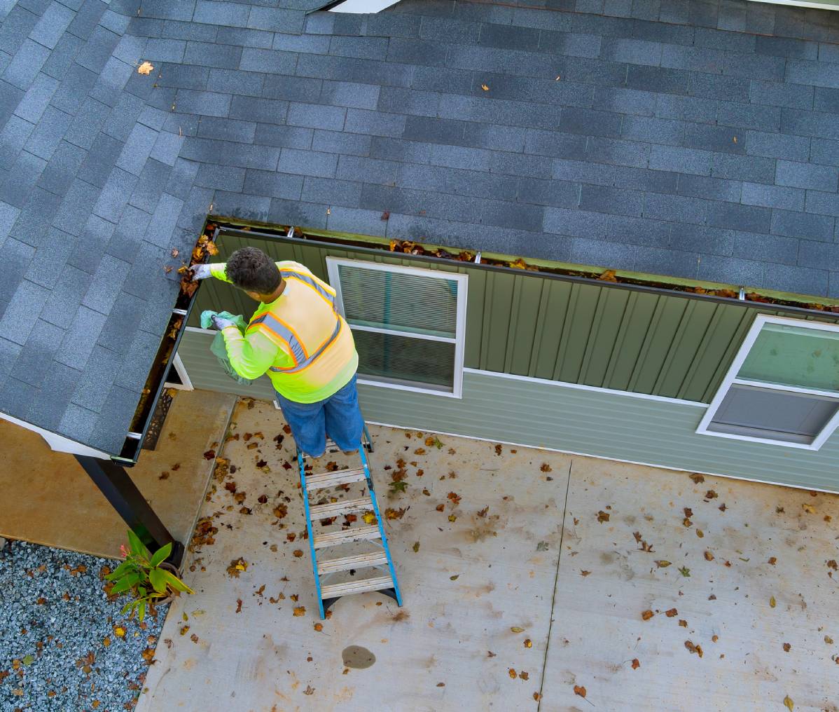 Worker clearing leaves from roof gutter