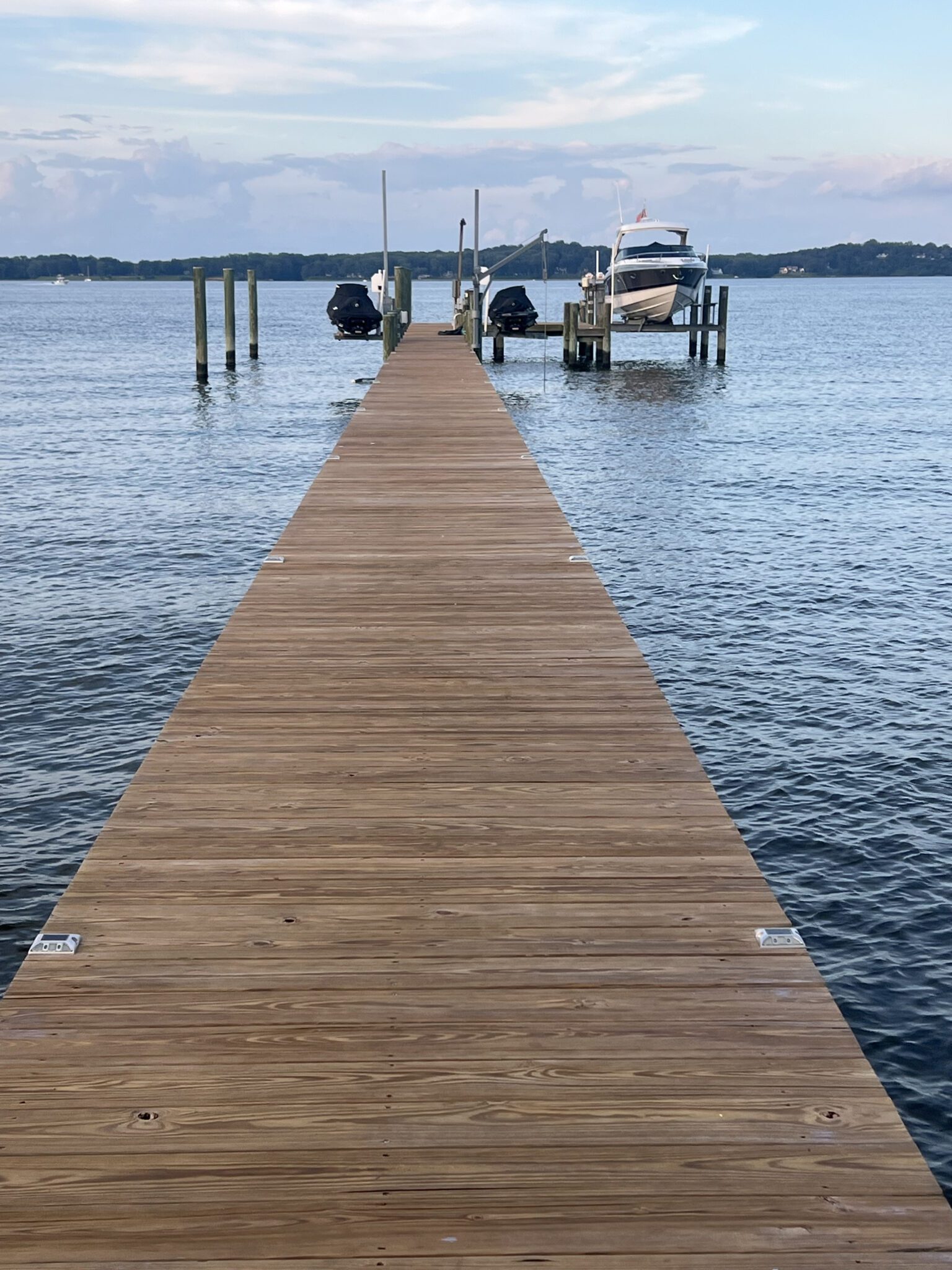 A wooden dock extending into calm water with boats moored at the end.