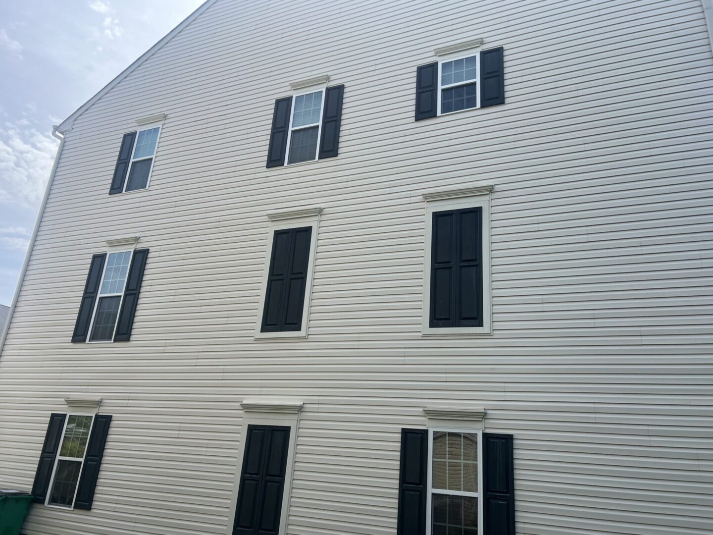 Exterior side of a white multi-story building with black window shutters.