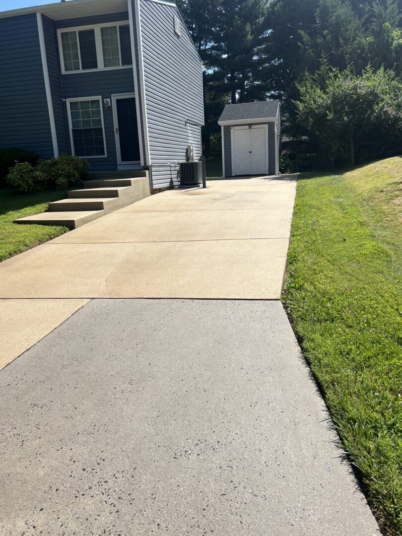 A clean driveway with a concrete walkway and green lawn beside it.
