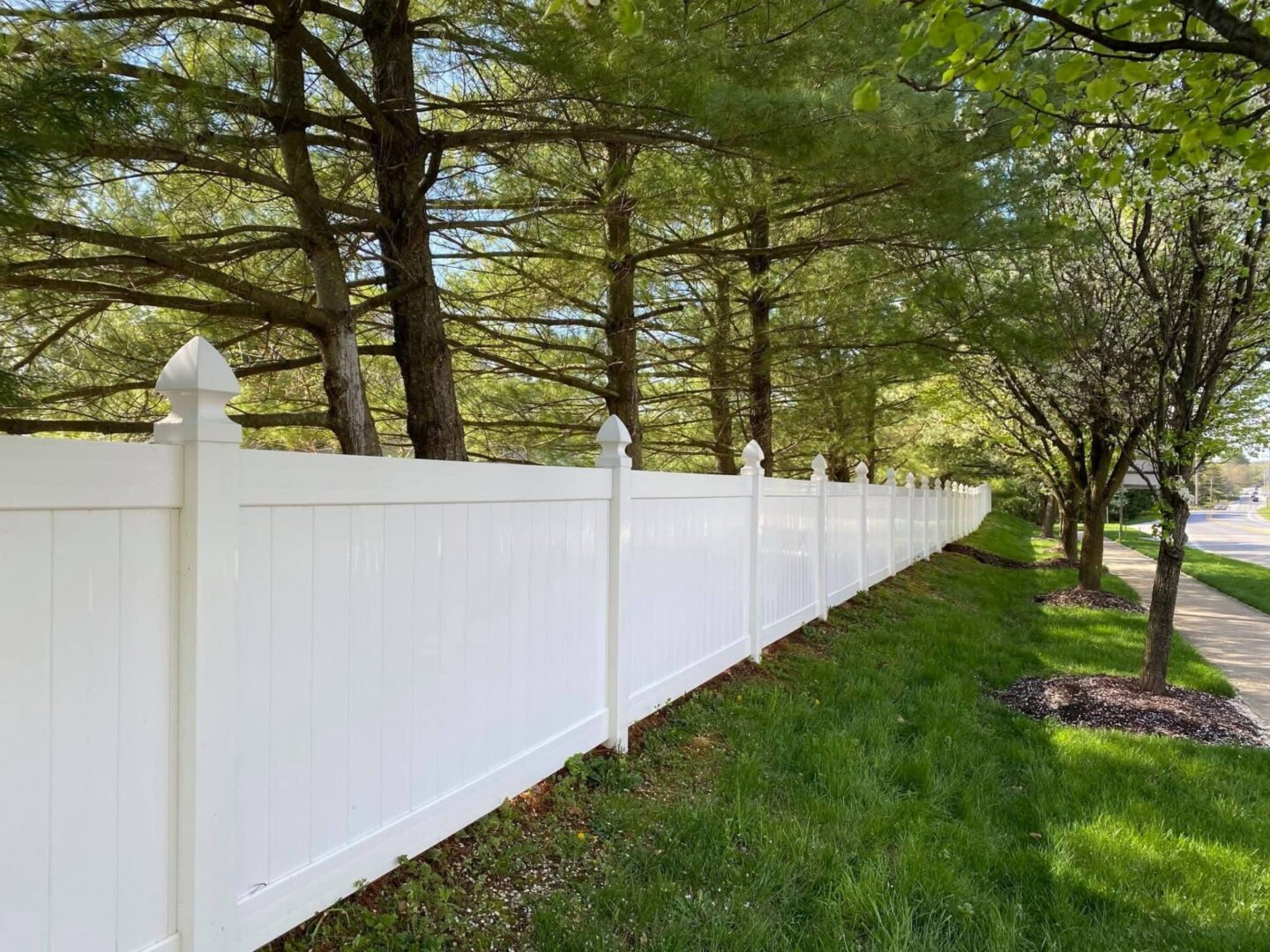 White vinyl fence alongside green grass and trees.